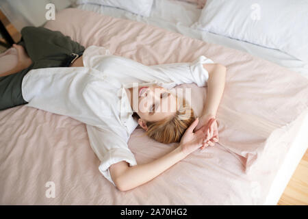 Donna bionda che indossa una camicia bianca giacente sul letto Foto Stock