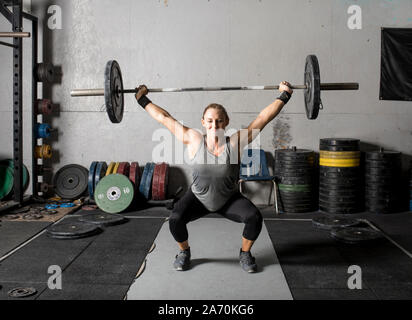 Vista frontale del forte giovane donna sollevamento pesi sopra la sua testa in palestra. Foto Stock