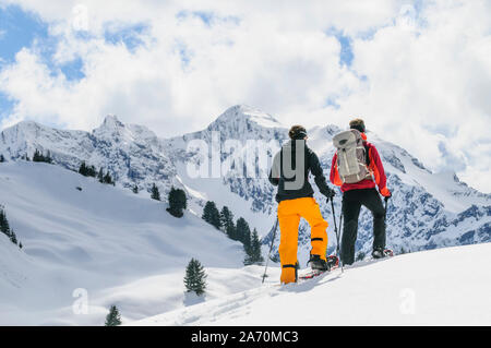 Coppia giovane escursionismo con le racchette da neve in una bella giornata nel tardo inverno Foto Stock