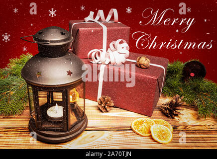 Due regali di Natale giacciono su di un tavolo di legno con una lanterna e un messaggio di saluto Foto Stock