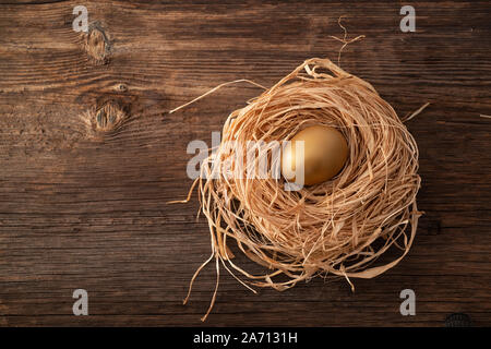 Unico e prezioso uovo dorato con nido su sfondo di legno Foto Stock