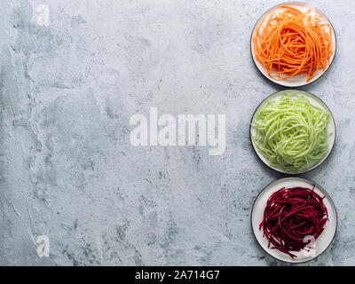 Tagliatelle di ortaggi - zucchine, carote e barbabietole noodles sulla piastra su cemento grigio Sfondo. Pulire mangiare vegetariano crudo, food concept. Copia spazio per il testo. Vista superiore piatta o laici. Foto Stock