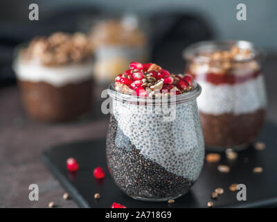 Colazione salutare concetto e idea - due colori chia pudding con materie organiche melograno, mandorla e grani di canapa. Il vasetto di vetro con il nero antracite e bianco latte vegano budino di Chia. Copia spazio per il testo Foto Stock