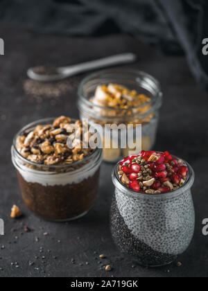 Set di chia pudding in differenti di vasetti di vetro scuro sul tavolo. Assortimento di chia puding con differenti di frutta,ingredienti. Copia spazio per il testo. Super,detox,sano pernottamento prima colazione concept Foto Stock