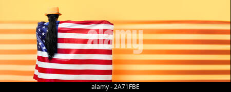 Ragazza sta con la schiena e tiene la bandiera americana su sfondo giallo, ragazza nel quartiere alla moda di hat con bandiera degli Stati Uniti, panoramica mock up immagine Foto Stock