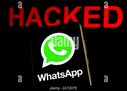 Logo WhatsApp sullo schermo dello smartphone in una stanza buia e la parola 'violato' a sfondo sfocato. Messa a fuoco selettiva. Foto Stock