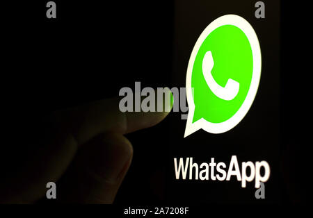 Logo WhatsApp sullo schermo dello smartphone in una stanza buia e un dito puntato a. Foto Stock