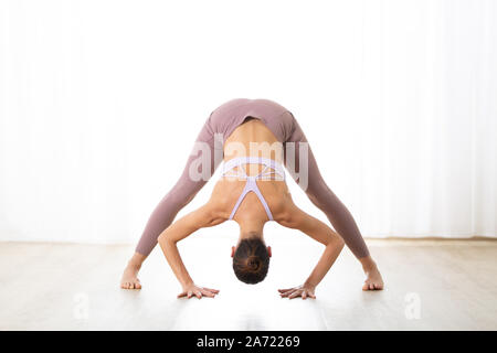 Ritratto di splendida sportiva attiva giovane donna a praticare yoga in studio. Bella ragazza pratica Dandayamana Bibhaktapada Paschimotthanasana Foto Stock