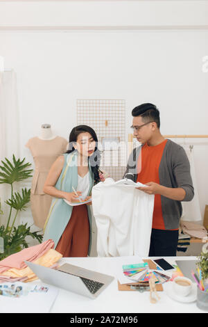 Parlando di nuovi design di moda. Giovane e bella donna che parla con il suo partner mentre si lavora insieme in officina Foto Stock