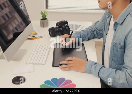 Fotografo il disegno e il ritocco immagine sul computer portatile, utilizzando una tavoletta digitale e penna stilo. Primo piano della mano d'uomo con fotocamera DSLR in backgro Foto Stock