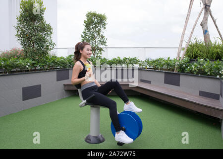 Donna che esercitano con attrezzature ginniche nel parco pubblico con detox di acqua in bottiglia in mano Foto Stock