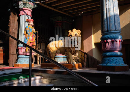 La luce del sole della mattina presto cade all'ingresso di un piccolo tempio di Krishna nella zona di Bhuleshwar di Mumbai, India, sorvegliata da figure di un leone e di un soldato Foto Stock