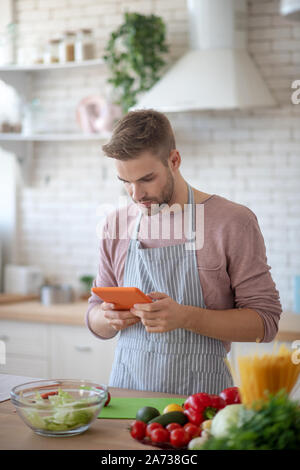 Uomo di guardare video su tablet e la cottura durante il fine settimana Foto Stock