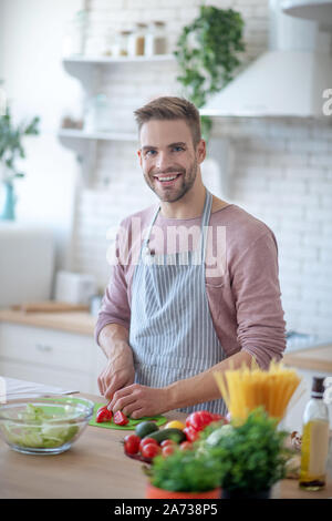 Bello blue-eyed uomo sorridente mentre cena di cucina Foto Stock