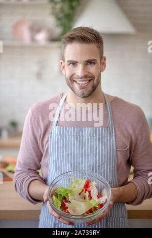 Allegro uomo che mostra la coppa con squisita insalata di verdure Foto Stock