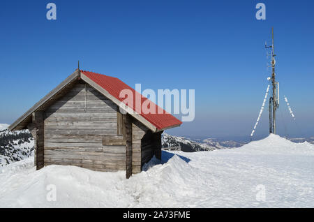 Alla fine dell'inverno, rifugio di legno e antenna sulla parte superiore della mountin, giornata di sole e neve di fusione Foto Stock