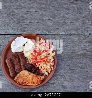 Sano e gustoso piatto forte, bistecca di pollo e fegato, cevapcici, formaggio e insalata in marrone piastra ceramica sul vecchio tavolo in legno di quercia, vista dall'alto Foto Stock