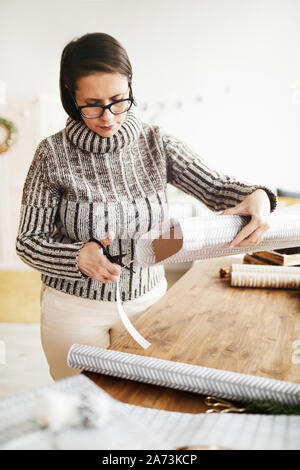 Giovane donna in occhiali in piedi e il confezionamento confezione regalo in carta da regalo per Natale Foto Stock