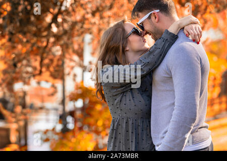 Felice amorevole coppia giovane in un abbraccio sorridente in ogni altri occhi contro un colorato autunno sfondo Foto Stock