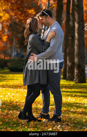 Felice coppia giovane con la moglie incinta abbracciando in un colorato parco autunno nella luce della sera Foto Stock