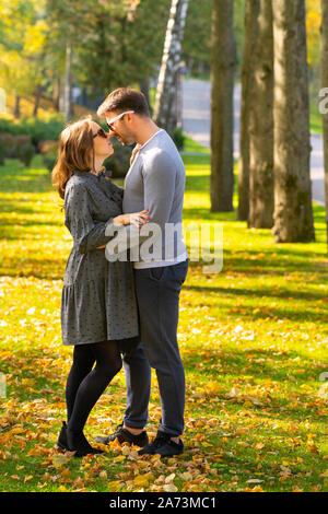 Amorevole alla moda giovane coppia in un parco d'autunno in piedi in un abbraccio cercando in ogni altri occhi con amore Foto Stock