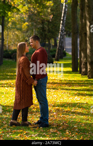 Due giovani di amore in piedi mano nella mano guardando in ogni altri occhi nella luce della sera in un parco in autunno Foto Stock