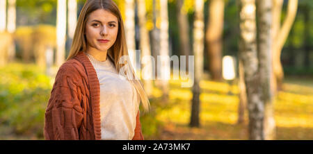 Panorama di una giovane e bella donna bionda in un autunno parco con colorate foglie gialle a terra girando di sorridere alla telecamera Foto Stock