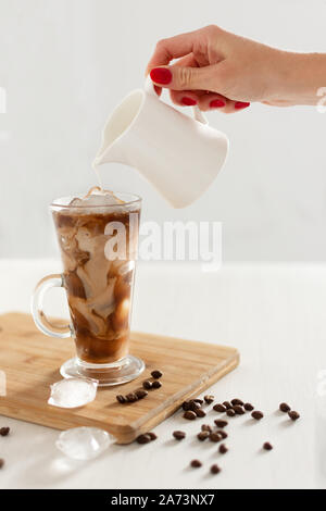 Caffè ghiacciato in un bicchiere con panna versato sopra. Caffè freddo con cubetti di ghiaccio e crema. Foto Stock