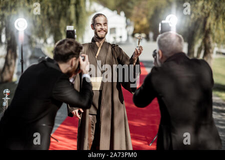 Uomo in costume come un ben noto personaggio del film a piedi con fastidiose foto Reporters sul tappeto rosso durante la cerimonia di premiazione Foto Stock