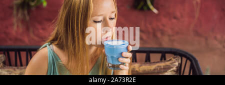 Giovane donna avente una colazione mediterranea seduto al divano e bevande bevanda alla moda: blu del latte. Hot butterfly pea latte o blue spirulina latte Foto Stock