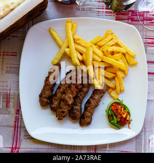 Piatto tradizionale della regione balcanica Cevapcici, grigliate le salsicce fatte di carni macinate servito con patate fritte e salse Foto Stock