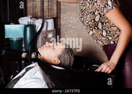 Bella donna bionda parrucchiere lava i capelli client nel salone di parrucchiere. Raddrizzatura di cheratina, tintura, cure e trattamenti termali. Foto Stock