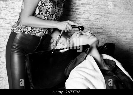 Primo piano di una femmina di parrucchiere lavando i capelli della ragazza bionda. Centro termale, bellezza, la cura e la salute dei concetti in bianco nero photo Foto Stock