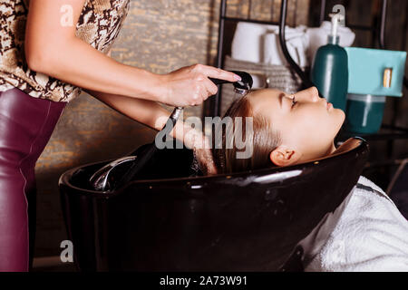 Bella donna bionda parrucchiere lava i capelli client nel salone di parrucchiere. Raddrizzatura di cheratina, tintura, cure e trattamenti termali. Foto Stock