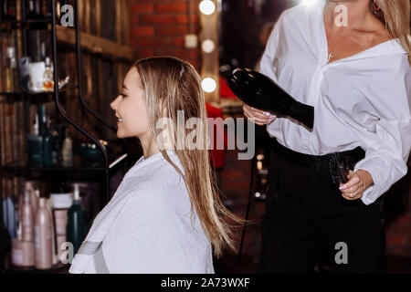 Carino bella parrucchiere rendendo acconciatura di giovane donna dopo il taglio di capelli in un salone di bellezza. Cura dei capelli, concetto di bellezza. Foto Stock