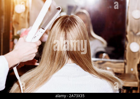 Chiusura del procedimento la raddrizzatura lunghi capelli biondi capelli con ferri da stiro. Bellezza, Hairstyle, hot styling, cheratina concetto di raddrizzatura. Parrucchiere rende h Foto Stock