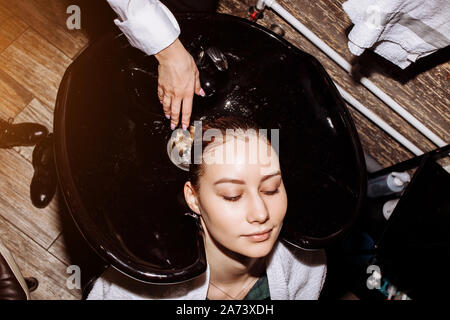 Primo piano volto del giovane e bella donna sorridente sempre cura dei capelli procedure in un salone di bellezza e i suoi occhi sono chiusi con il rilassamento. Cura dei capelli, bellezza pro Foto Stock