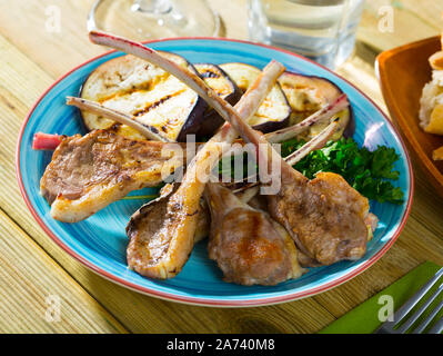 Gustose costolette di agnello alla griglia con melanzane alla piastra con verdi sul tavolo Foto Stock