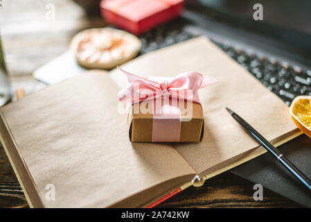 Confezione regalo con nastro rosa sul blocco note con il computer portatile. Sorprese inaspettate e desiderabile regali per Capodanno e Natale Foto Stock