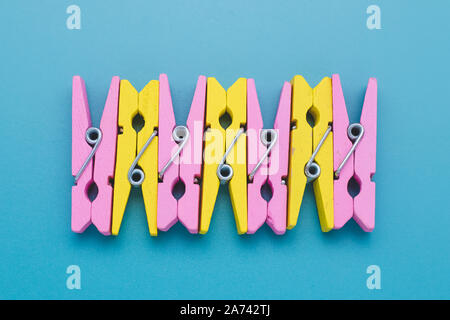 Concetto di divertimento dell'umore. In legno colorato clothespins su carta blu sullo sfondo. Creative design minimale. Giallo e rosa clothespin, abstract multicolor Foto Stock