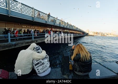 Coppia giovane seduto sul bordo d'acqua e guardando con vista sul mare vicino a ristoranti di pesce sotto il ponte Galata. Lonely donna sedersi accanto a loro. Foto Stock