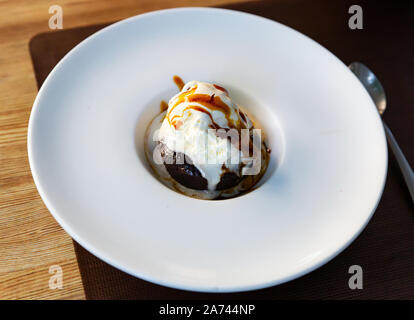 Delicato brownie al cioccolato servito con gelato e sciroppo di caramello sulla piastra bianca Foto Stock