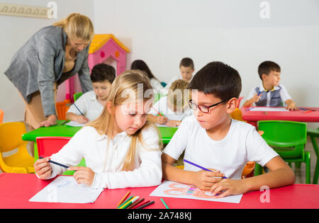 Felice di chattering alunni seduti a lezione a scuola elementare Foto Stock
