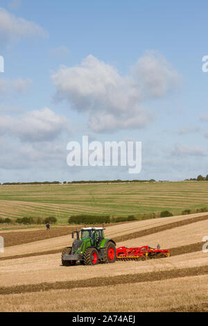 Un grande e moderno di colore verde trattore Fendt coltivare i campi in un match di aratura vicino Ipsden sul bordo del Chilterns con cielo blu e nuvole Cumulus Foto Stock