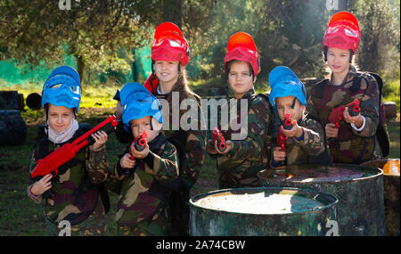 Gentile felice allegro sorridente gruppo di bambini paintball giocatori in camuffamento in posa con pistole di paintball sul campo da gioco all'aperto Foto Stock