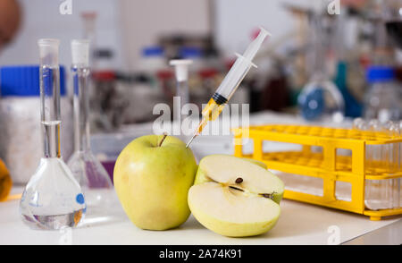 Siringa con additivo chimico in fresco di Apple su sfondo con attrezzature da laboratorio. Concetto di ricerca di cibo la modificazione genetica Foto Stock