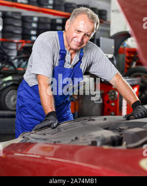 Esperto maturo mechanician auto cambio olio motore nel veicolo in un negozio di riparazioni auto Foto Stock