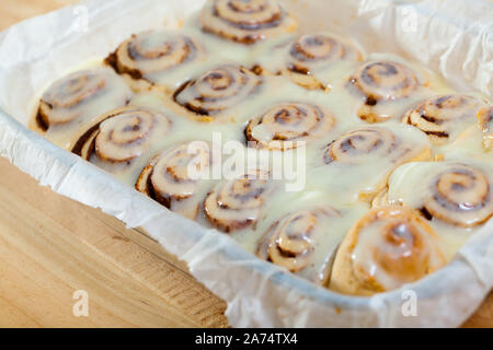 Appena sfornato cinnabons fatti in casa panini alla cannella con latte glassa di zucchero in una teglia Foto Stock