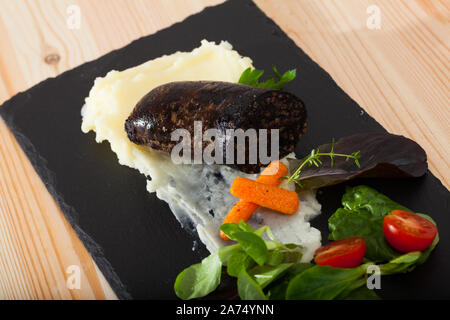 Black Pudding con riso servito con purè di patate, ortaggi e verdure su ardesia Foto Stock