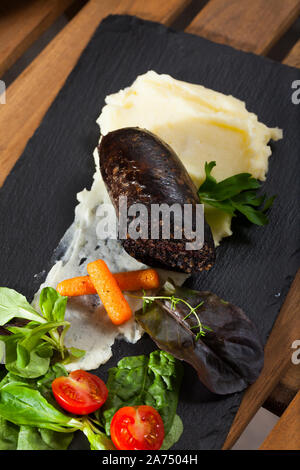 Spagnolo tradizionale salsiccia di sangue con riso servito con purea di patate, carote, pomodoro ciliegino e verdi Foto Stock